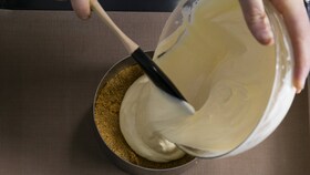 A baker pouring the smooth cheesecake mixture into a cake ring, ready for the oven